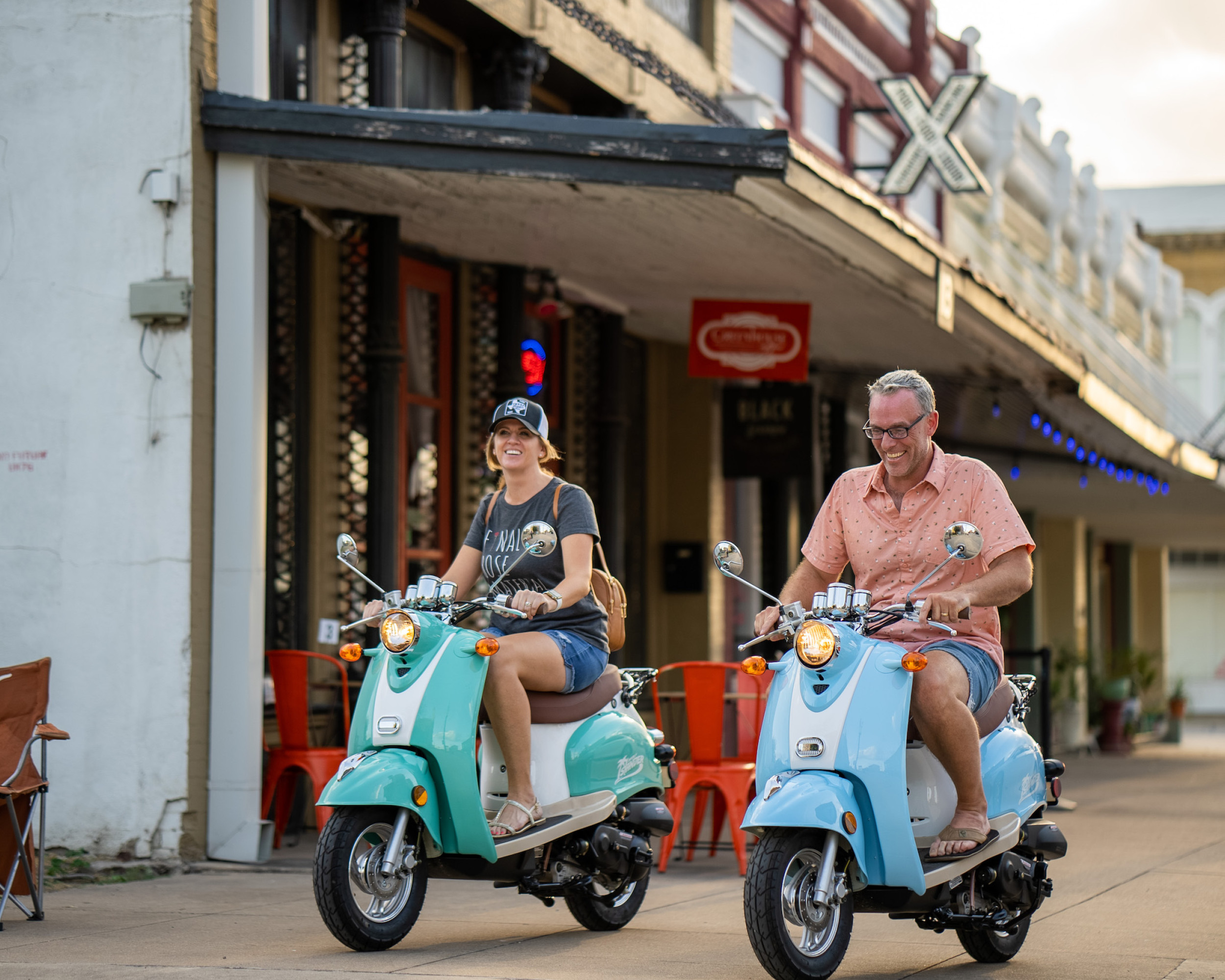 Two people riding mopeds through downtown Taylor
